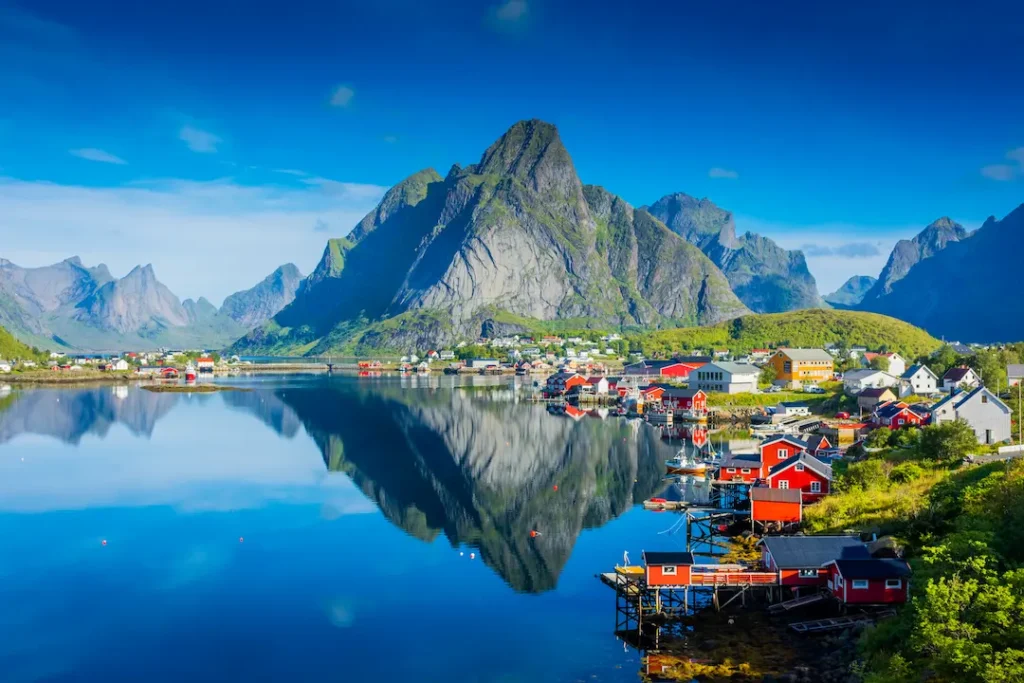 Coastal village with colorful houses at the water's edge, mountains reflected in calm harbor.