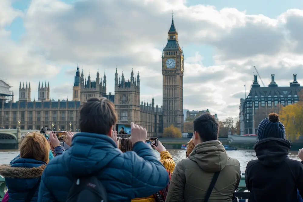 Tourists on the riverfront photographing Big Ben and the Palace of Westminster in London with their phones